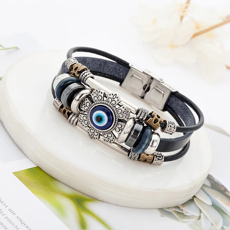 Multistrand bracelet with decorative clasp and blue evil eye charm on a white stone surface.