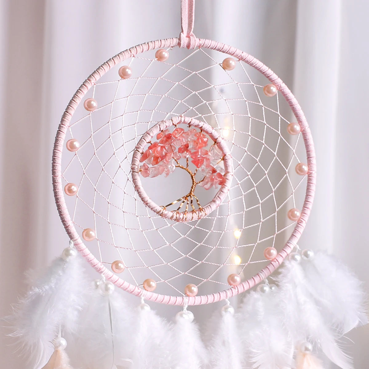 Pink dreamcatcher with feathers against a white background