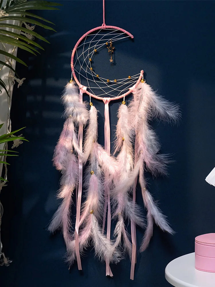Pink dreamcatcher with feathers against a dark blue wall