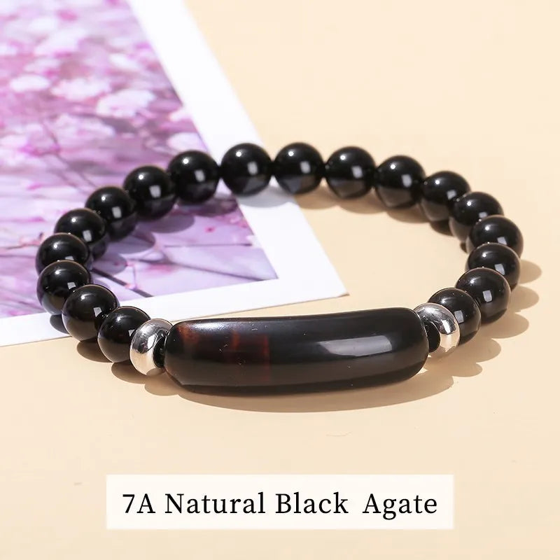 Black agate beaded bracelet on a beige surface with a pink floral background
