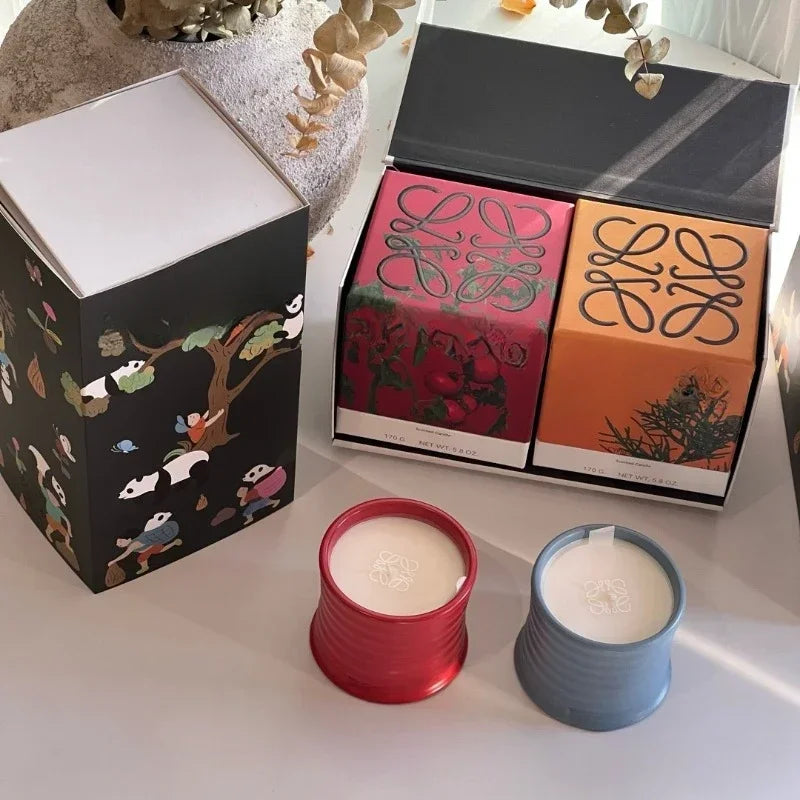 Two candles in red and blue holders with decorative boxes in the background.