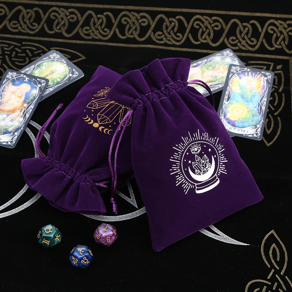 Two purple drawstring bags with mystical designs on a black background with tarot cards and dice.