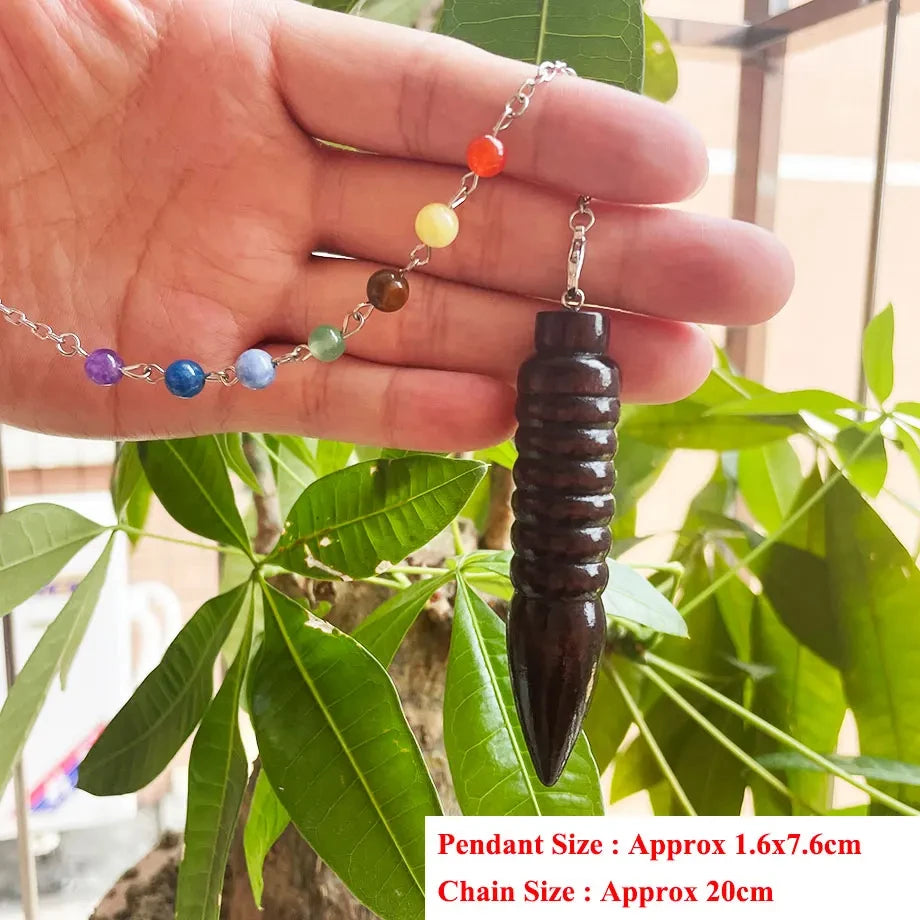 Hand holding a black pendant with colorful beads against a green leafy background