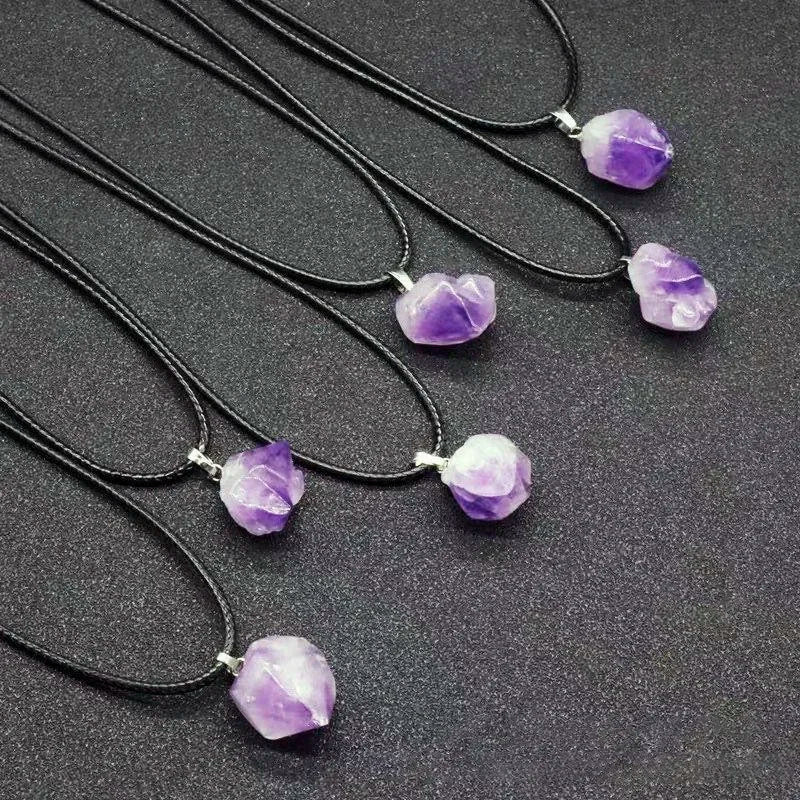 Necklaces with purple crystal pendants on black cords against a dark background