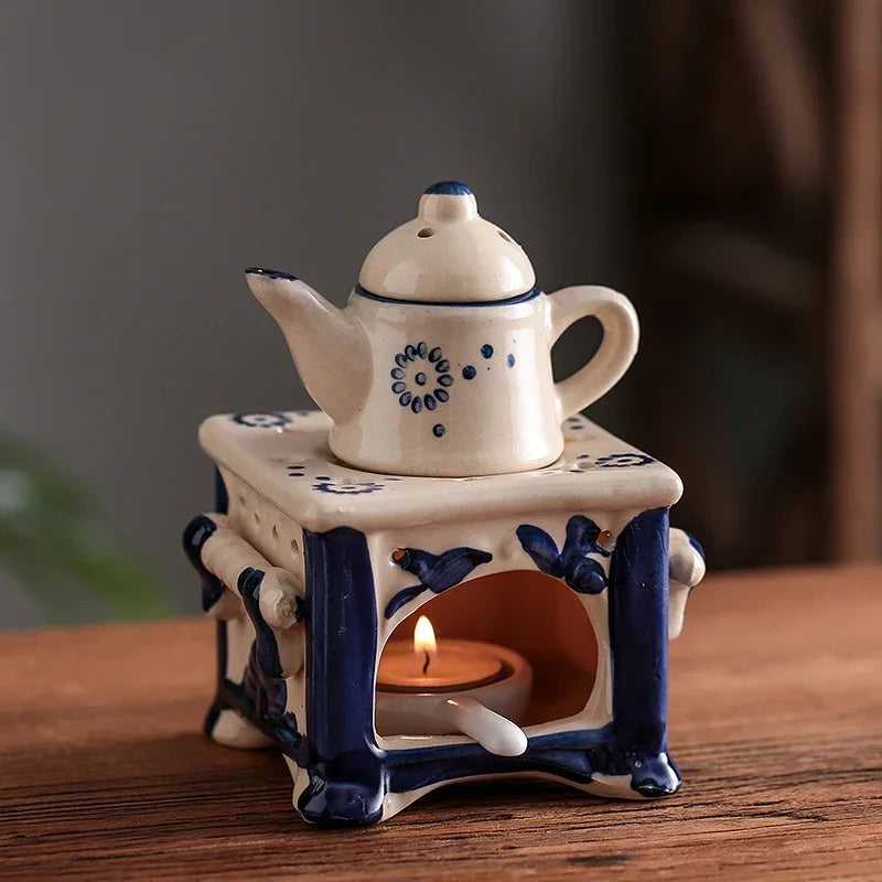 Ceramic teapot with decorative elements on a small stove-like structure with a candle inside, on a wooden surface.