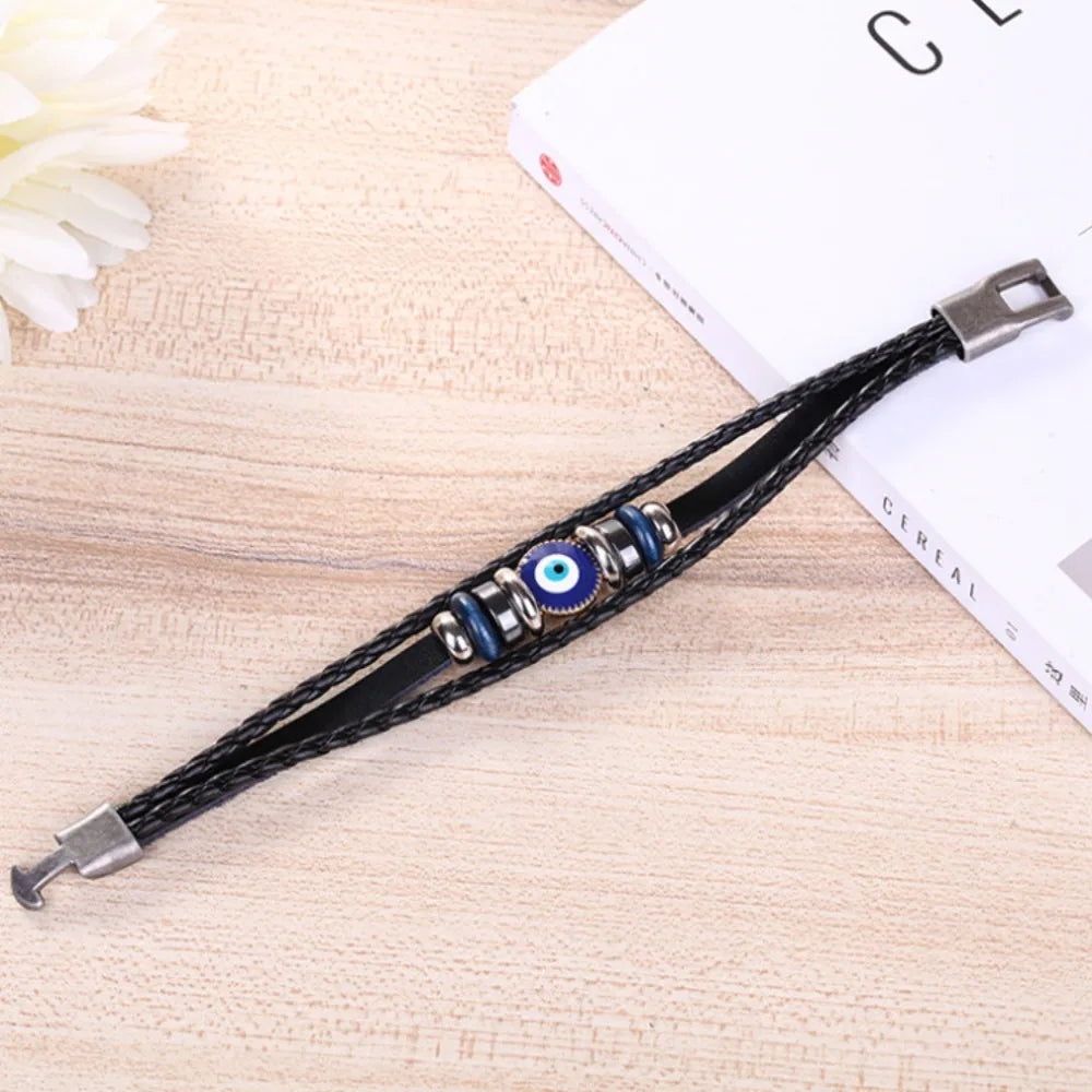 Black leather bracelet with blue evil eye charm on a wooden surface