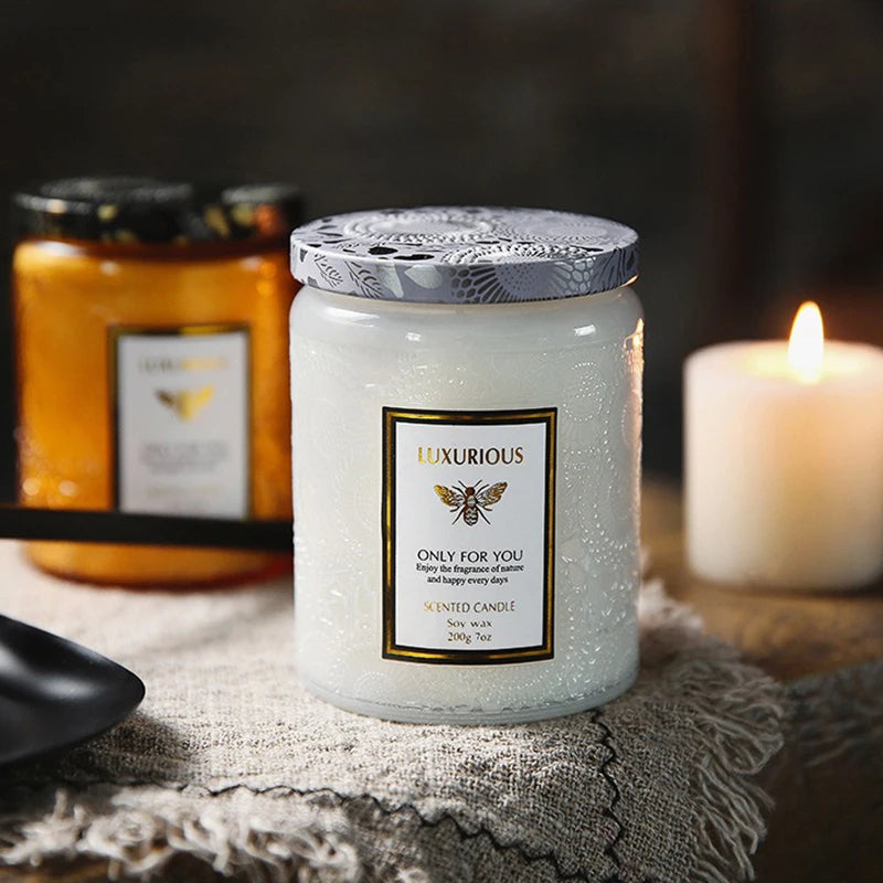 Luxurious scented candle with decorative label on a textured surface, with another candle and jar in the background.