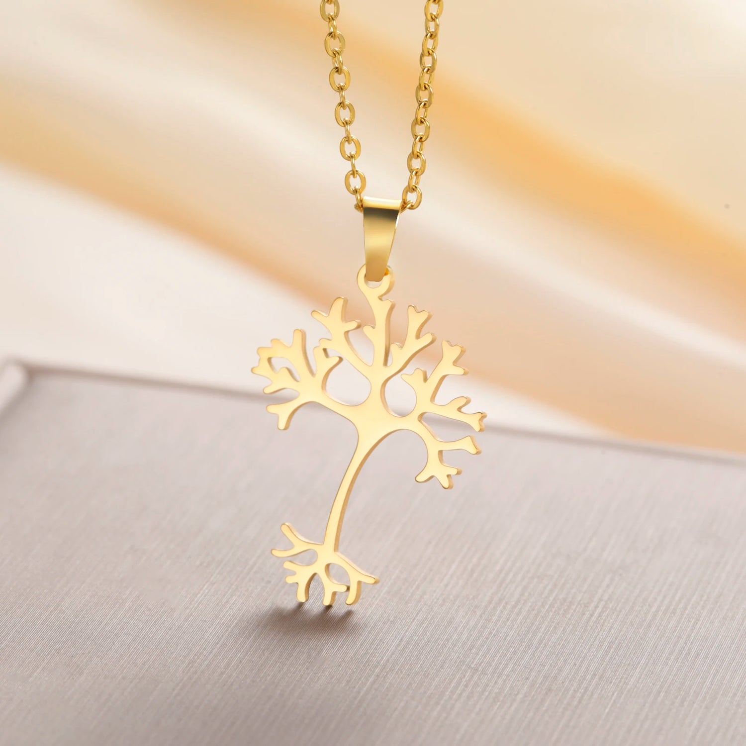 Gold tree-shaped pendant necklace on a soft gradient background