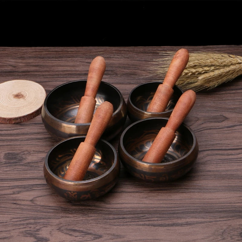 Set of four bronze singing bowls with wooden mallets on a wooden surface.