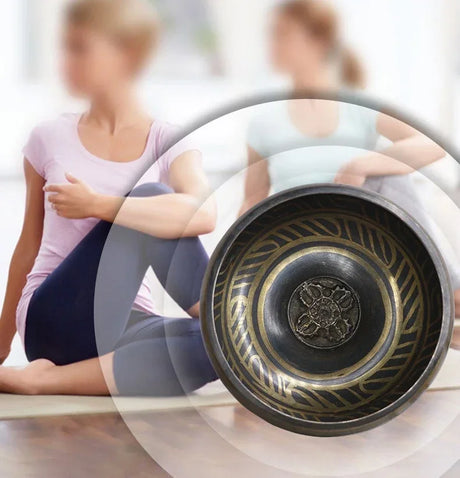 Close-up of a decorative metal bowl with intricate designs, blurred background of people sitting on the floor.