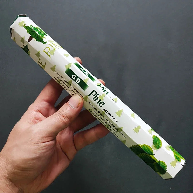 Hand holding a pack of 'GR Pine' incense sticks against a dark background