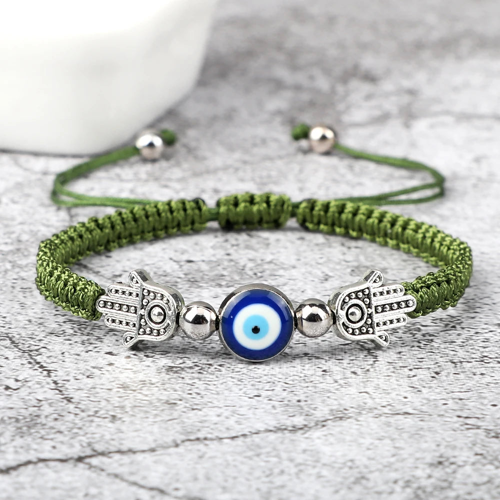 Green braided bracelet with Hamsa hand and evil eye charm on a gray surface
