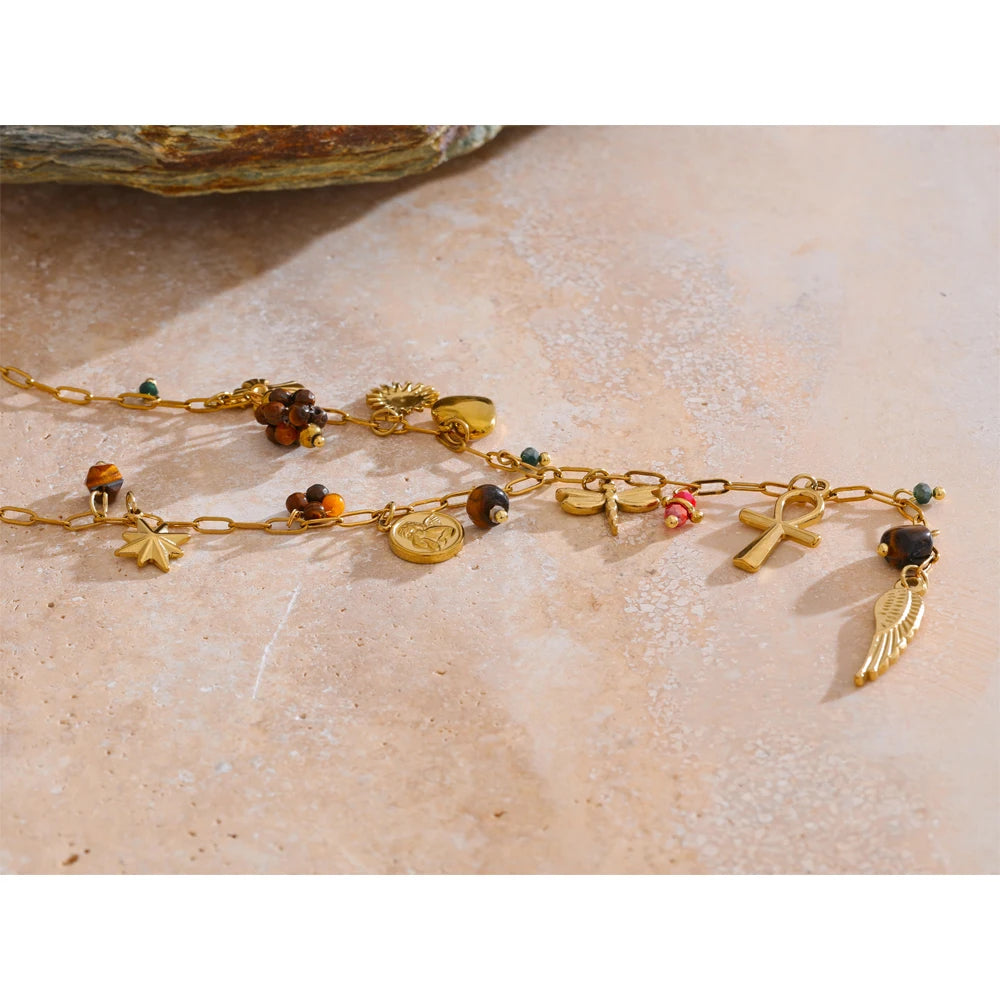 Gold anklet with various charms on a textured beige surface