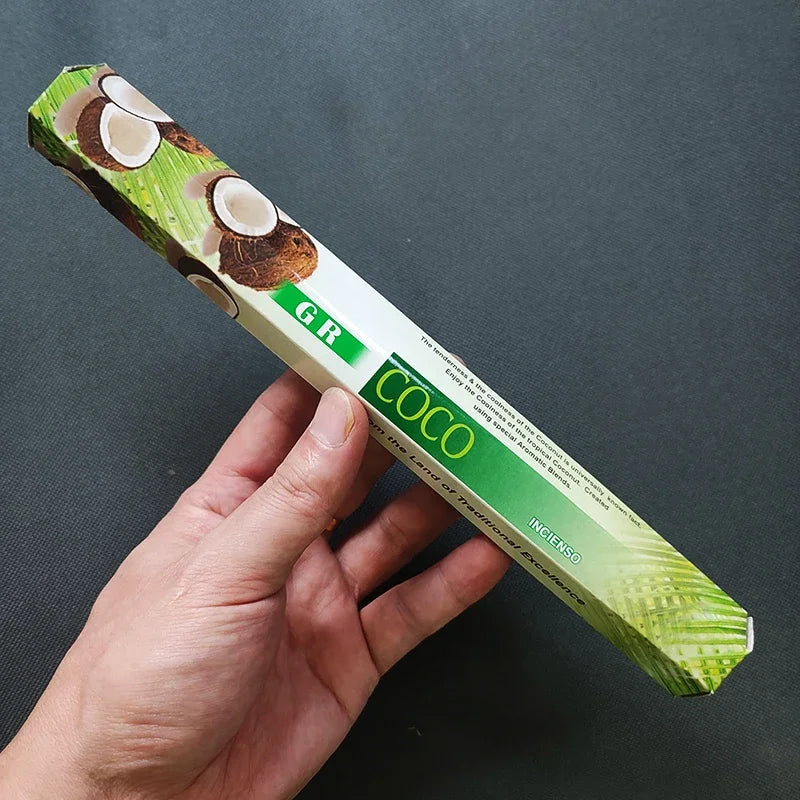 Hand holding a green incense stick box with coconut design on a dark background
