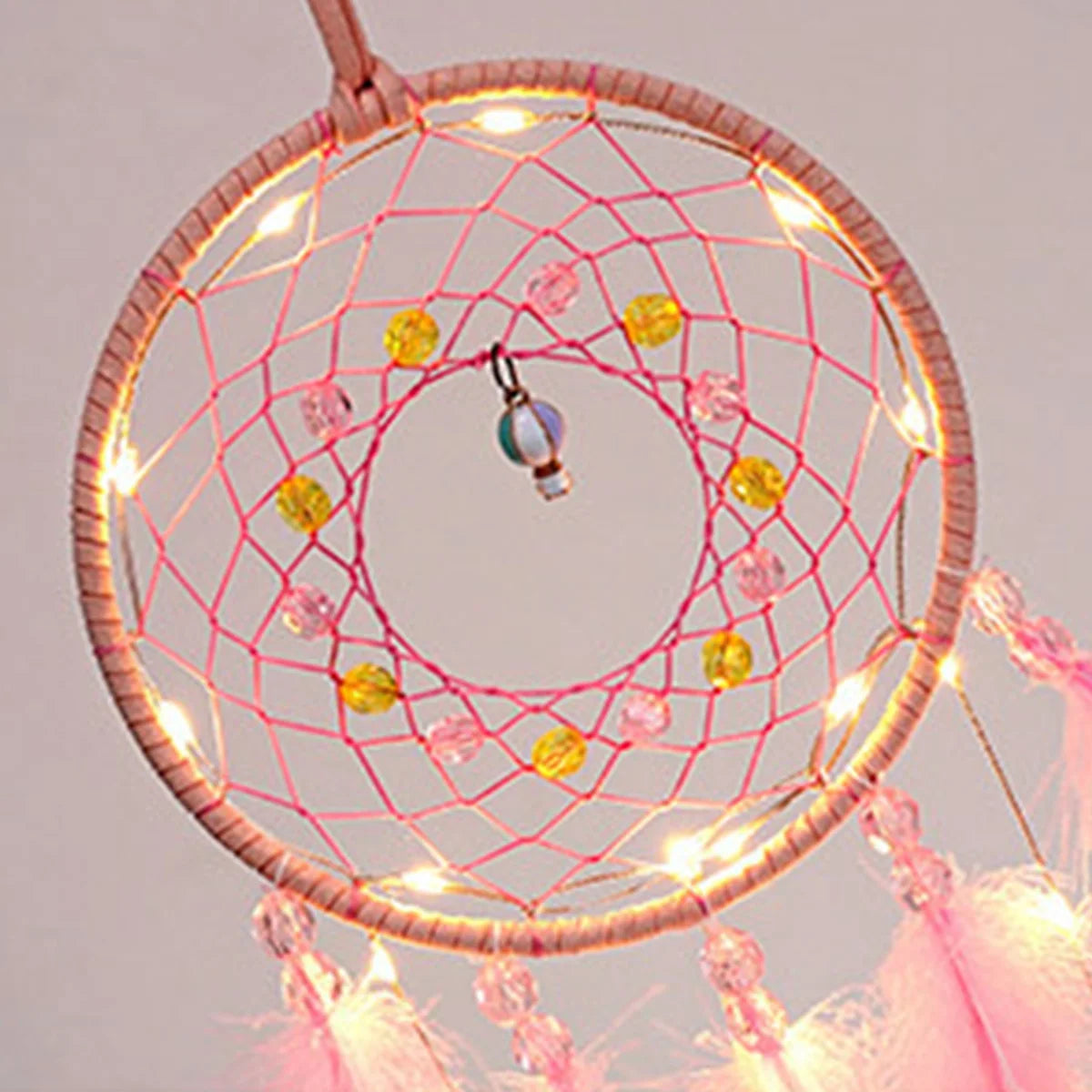 Decorative dreamcatcher with pink netting, colorful beads, and fairy lights on a light gray background