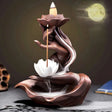 Ceramic incense burner shaped like a lotus flower with a candle on a dark background.