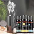 Mayjam essential oil diffuser with smoke and bottles labeled Eucalyptus, Chamomile, and Jasmine on a wooden surface.