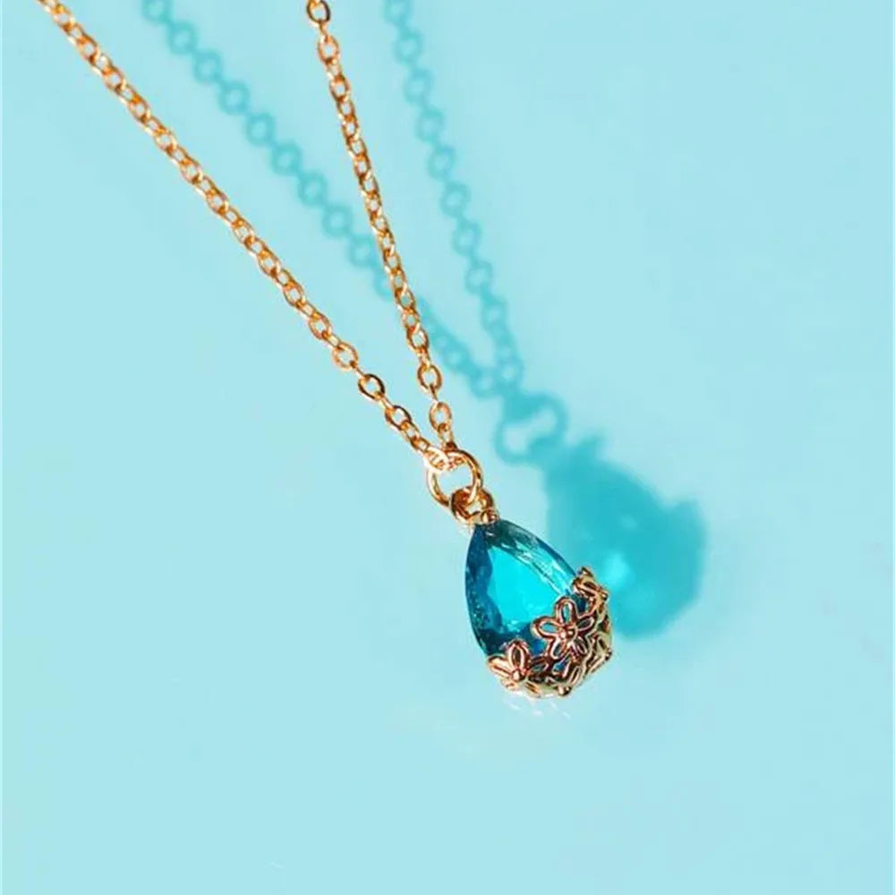 Gold necklace with a blue teardrop pendant on a light blue background