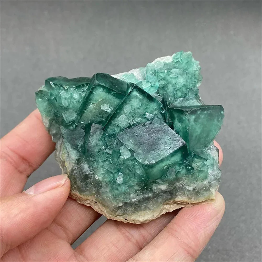 Green crystal rock held in a hand against a gray background