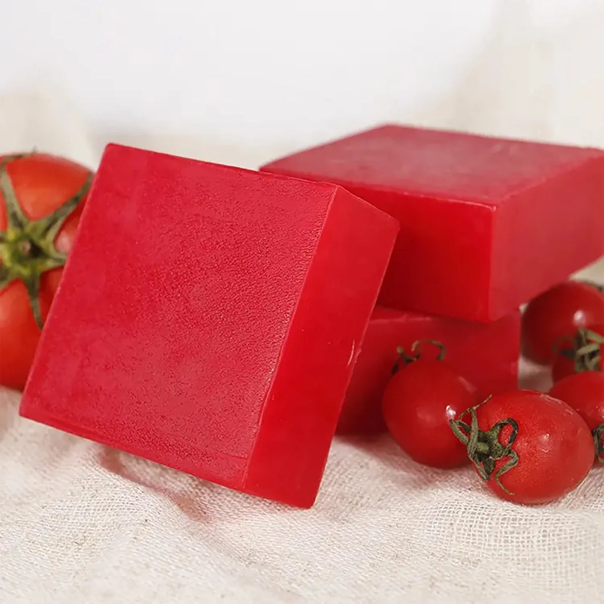 Red soap bars with small tomatoes on a light fabric background