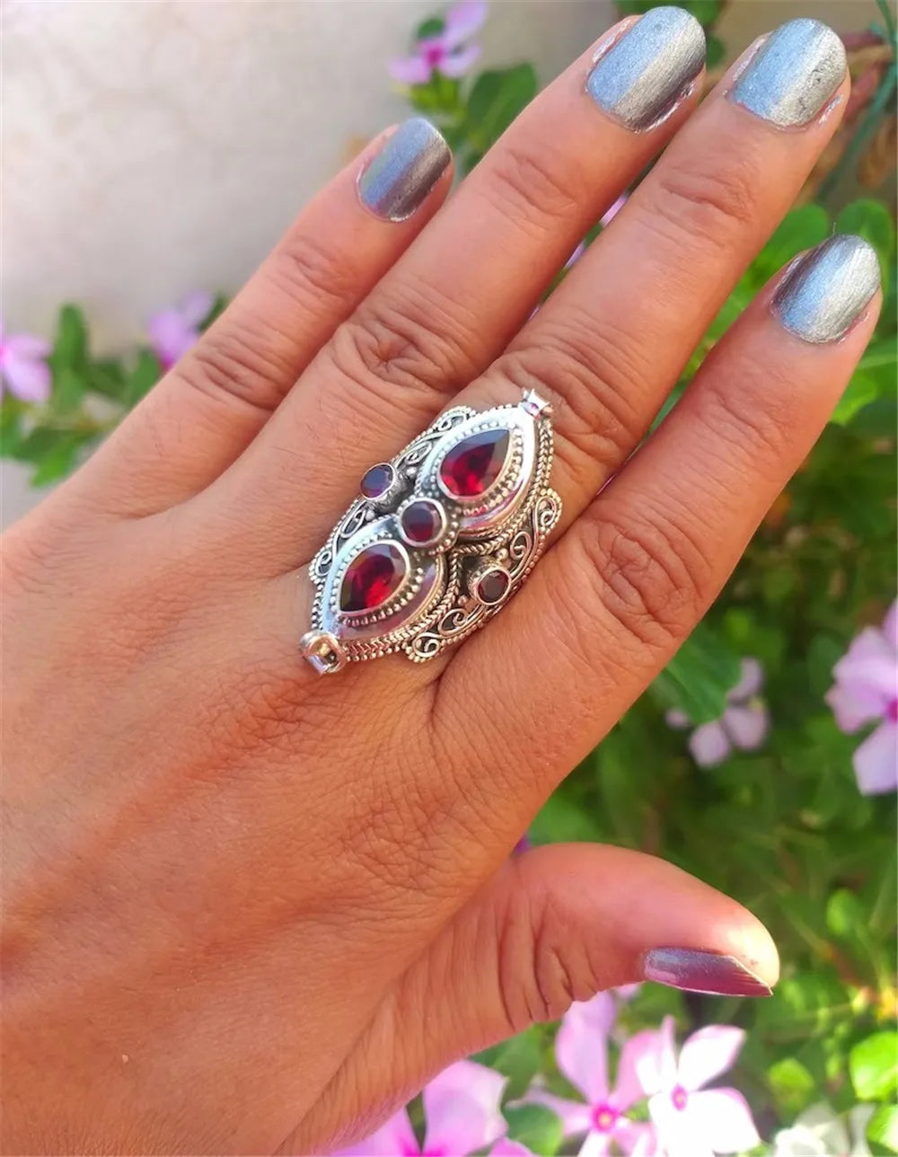 Hand wearing a decorative ring with gemstones against a blurred natural background