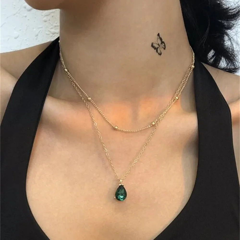 Gold necklace with a green pendant worn by a person against a neutral background