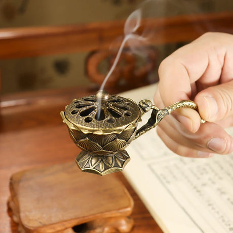 Bronze incense burner with a hand holding it, set against a wooden background.