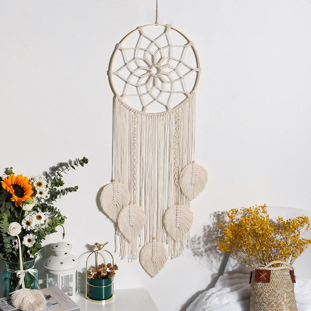 Beige dreamcatcher with heart-shaped elements on a white wall, surrounded by decorative plants.