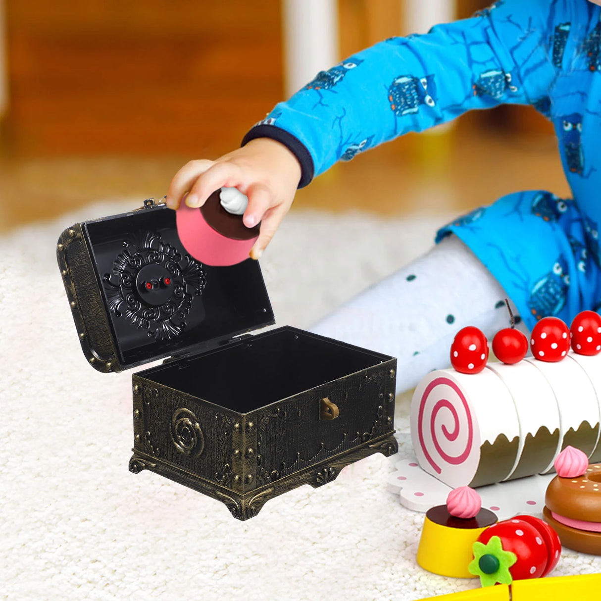 Child playing with a toy music box and cake figurines on a soft surface.