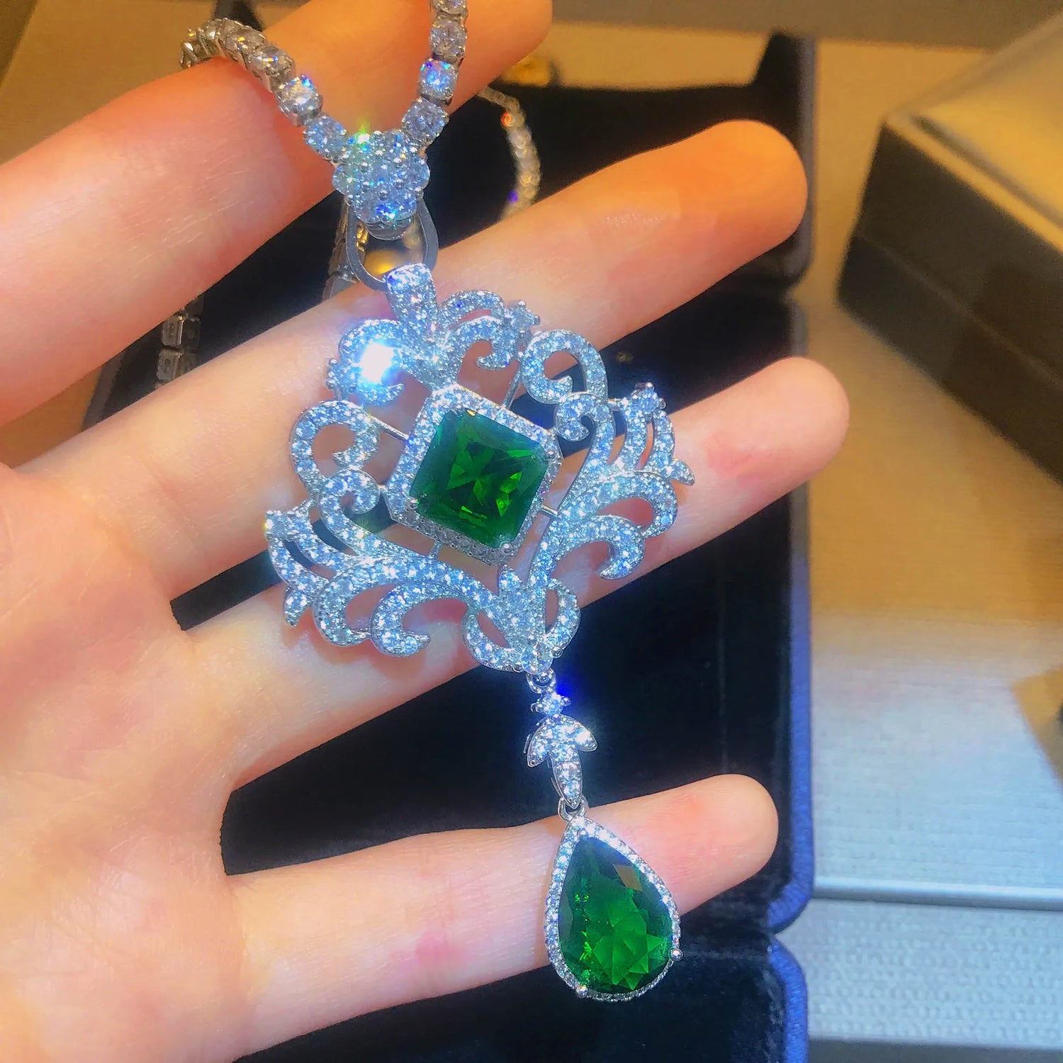 Elegant silver pendant with green gemstones held in a hand