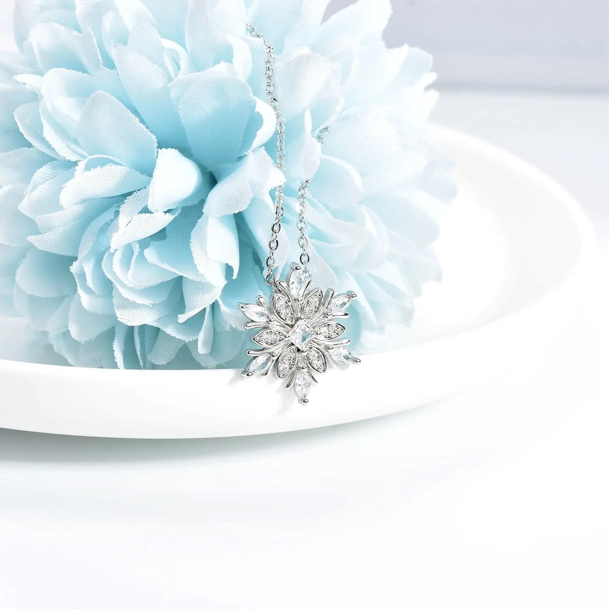 Silver snowflake pendant necklace on a light blue flower