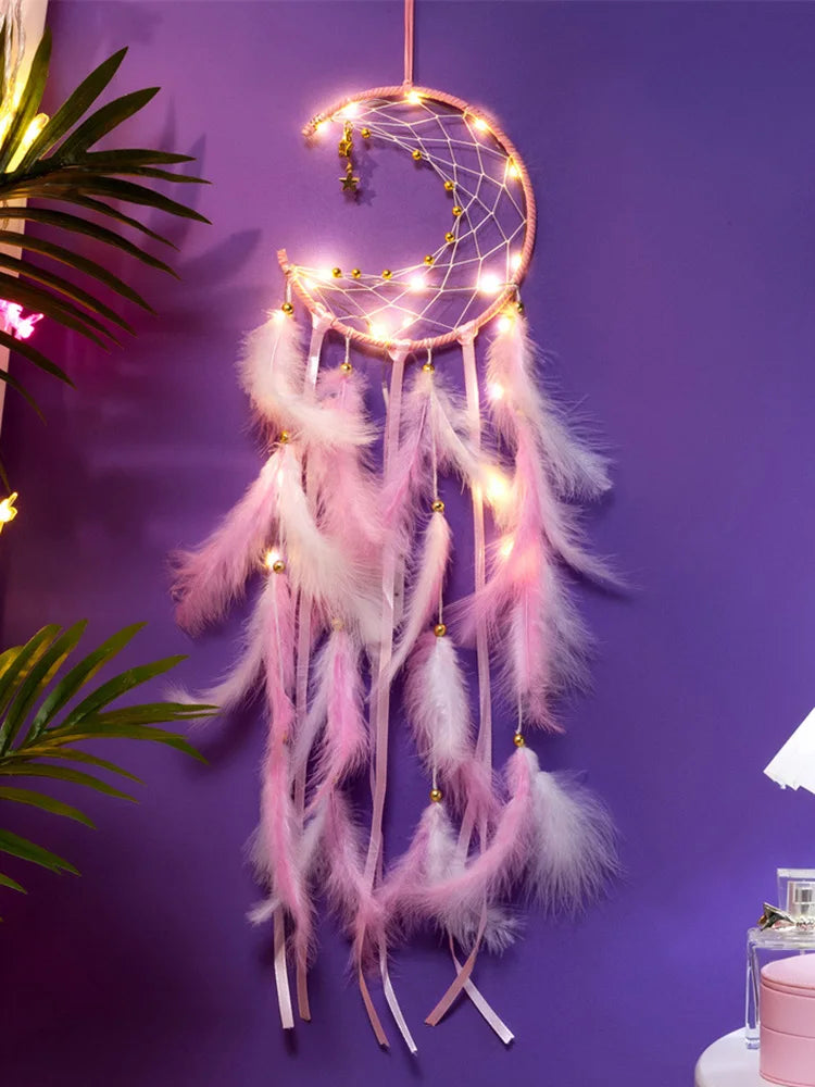 Decorative dreamcatcher with pink feathers and string lights against a purple wall.