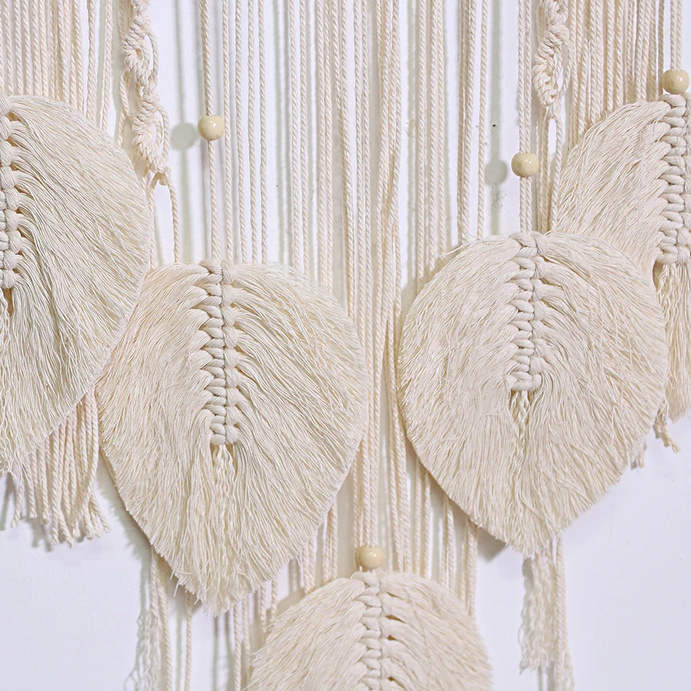 Close-up of a macrame wall hanging with beige threads and wooden beads on a white background
