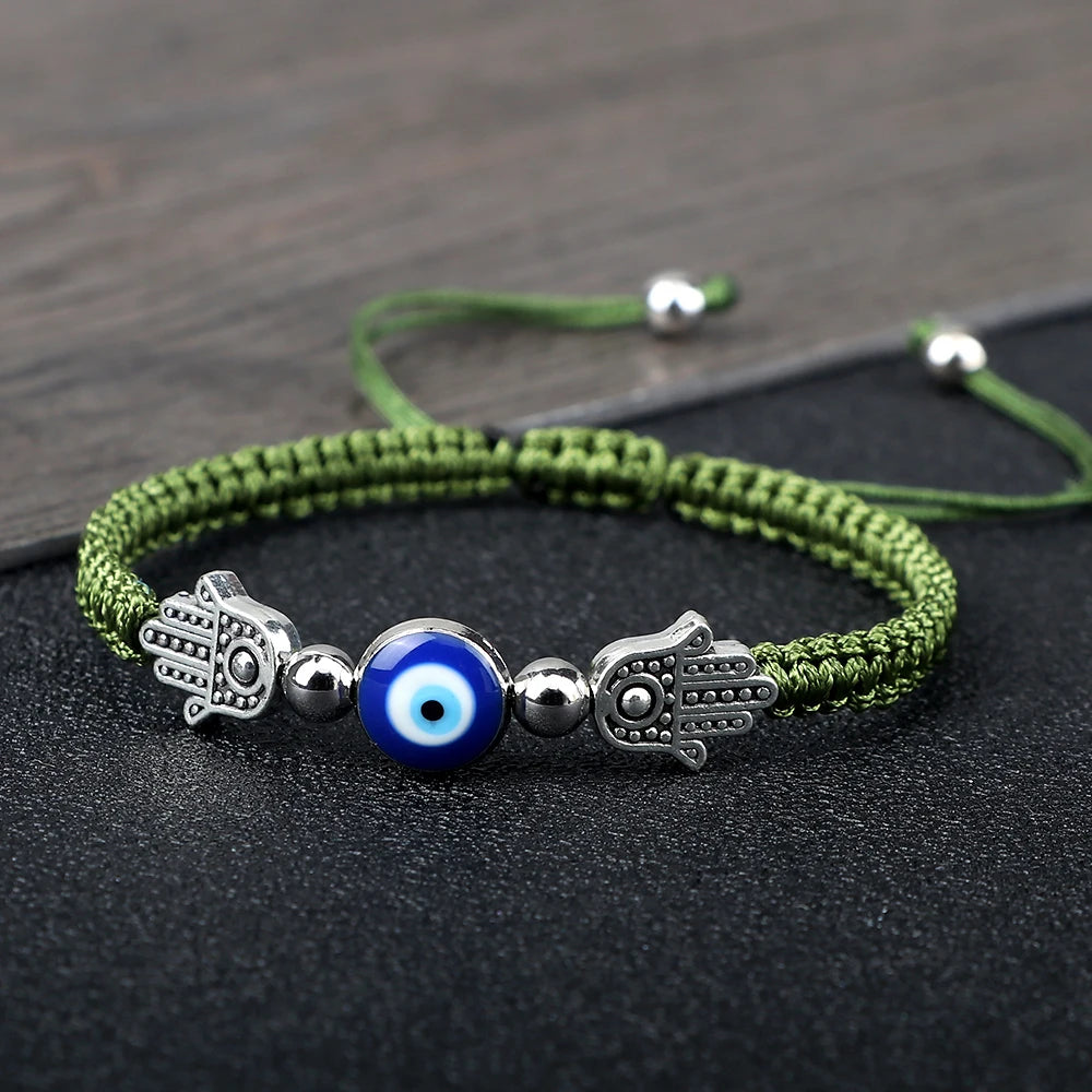 Green bracelet with blue evil eye charm and silver hamsa hand on a dark surface