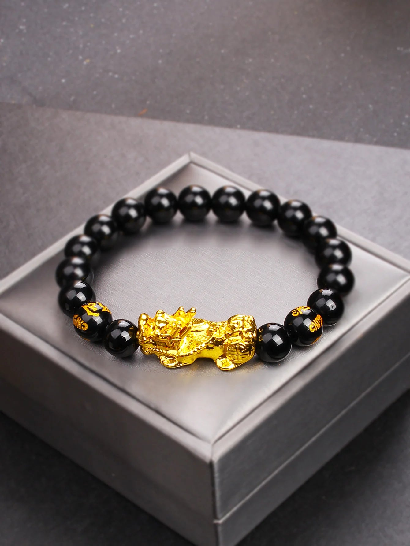 Black beaded bracelet with a gold dragon charm on a gray box