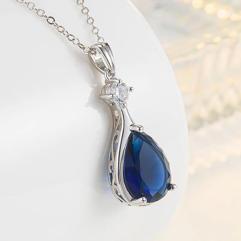 Silver pendant with a blue teardrop-shaped gemstone on a white background