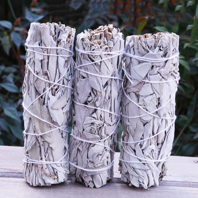 Three bundles of sage tied together with twine on a wooden surface with a natural background.