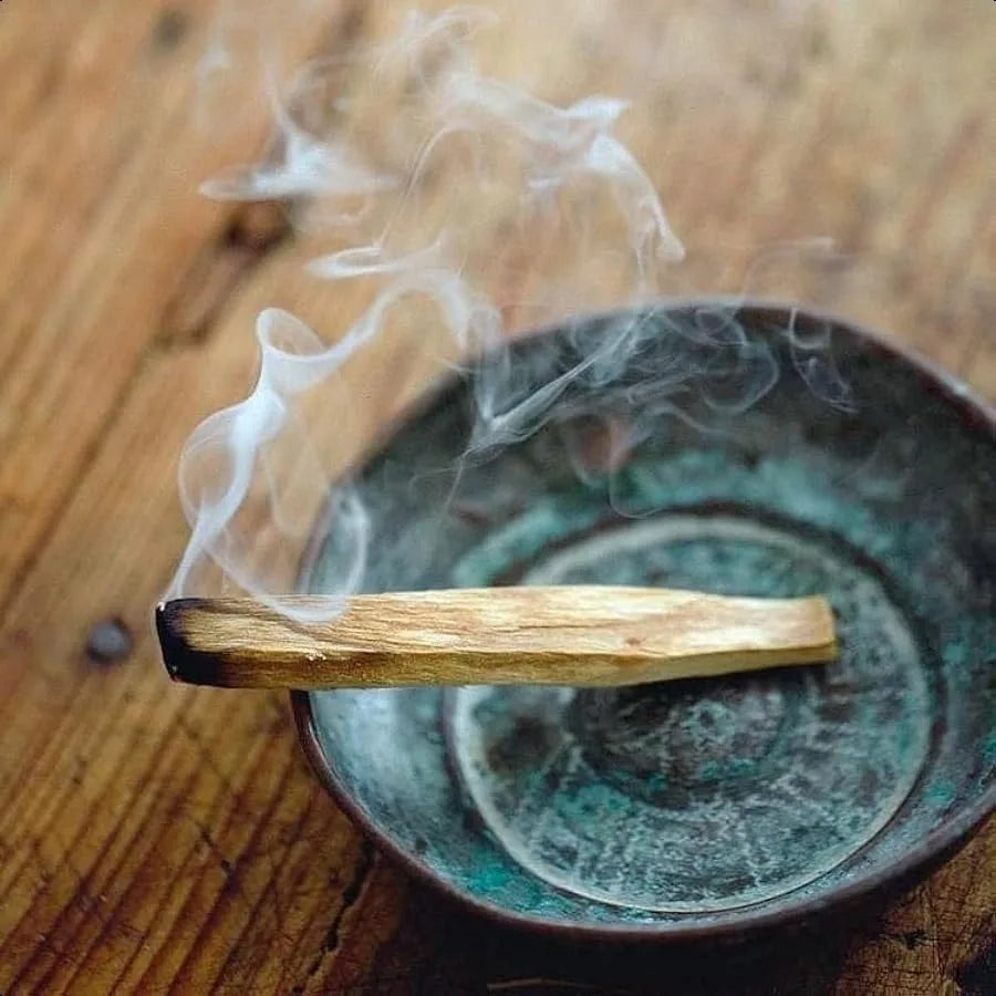 Incense stick with smoke over a ceramic dish on a wooden surface