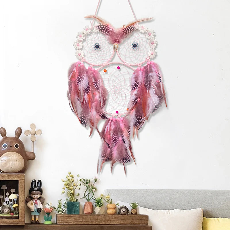 Pink owl-shaped dreamcatcher hanging on a white wall above a shelf with decorative items.