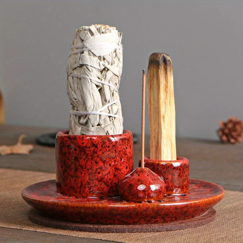 Red ceramic holder with sage, incense sticks, and a crystal on a wooden surface.
