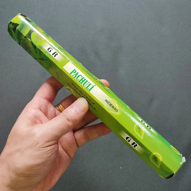 Hand holding a green Pachulí incense stick packaging against a gray background