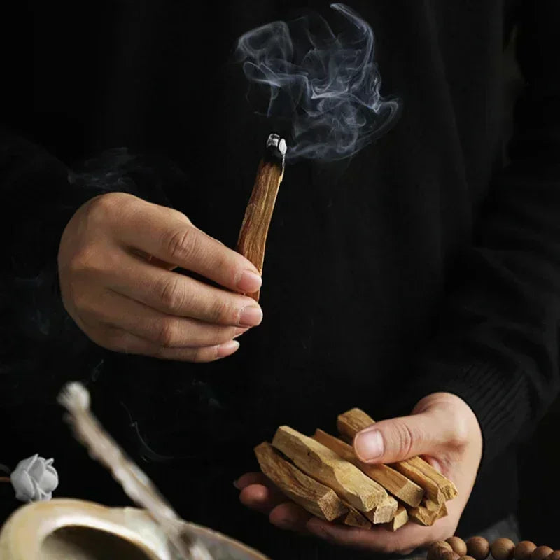 Hands holding a smoking Palo Santo Holy Wood Natural Incense Stick during a smudging ritual.