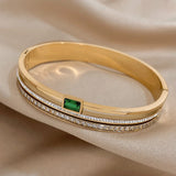 Gold bracelet with emerald and diamonds on a beige fabric background