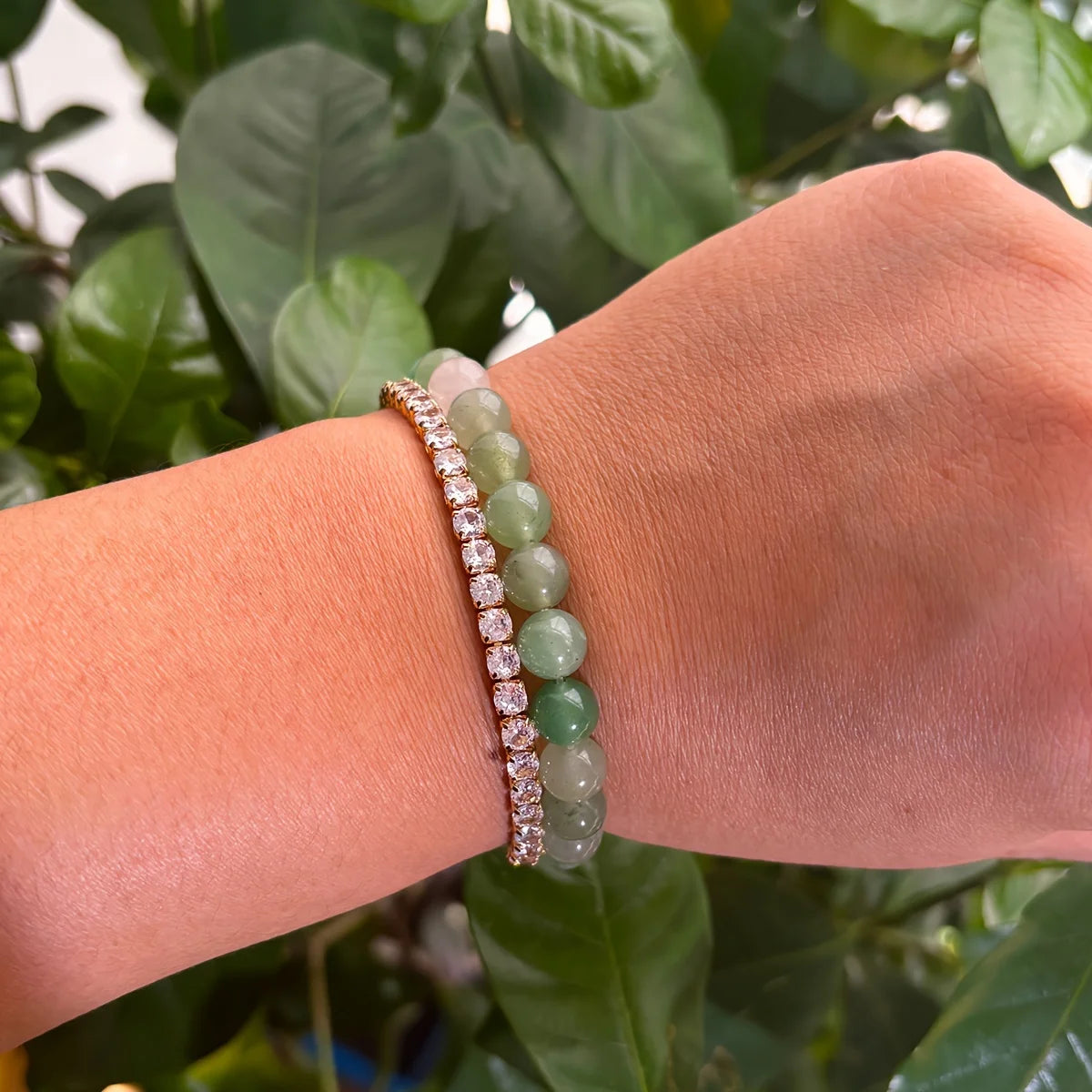 Hand wearing two bracelets with a green leafy background