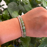 Hand wearing two bracelets with a green leafy background