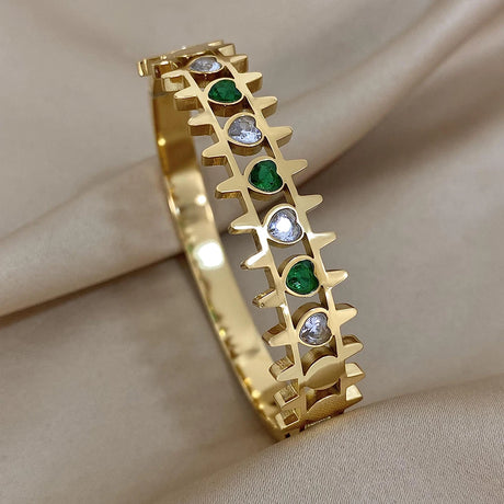 Gold bracelet with green and silver gemstones on a beige fabric background