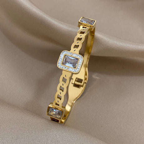 Gold bracelet with square gemstones on a beige fabric background