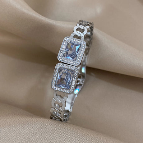 Silver bracelet with square-cut gemstones on a beige fabric background