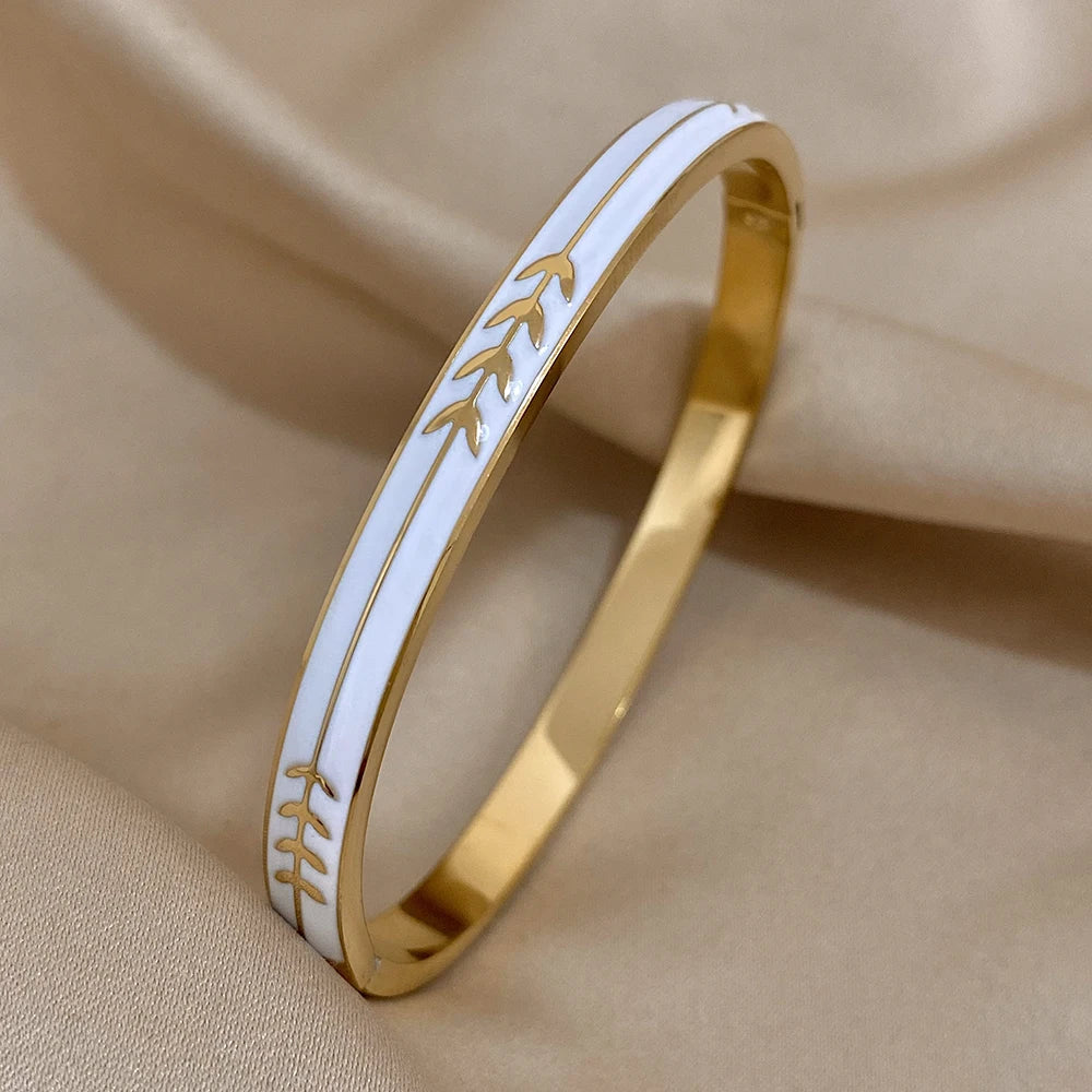Gold bracelet with white band featuring leaf pattern on beige fabric background