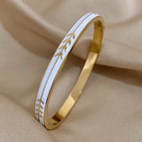Gold bracelet with white band featuring leaf pattern on beige fabric background